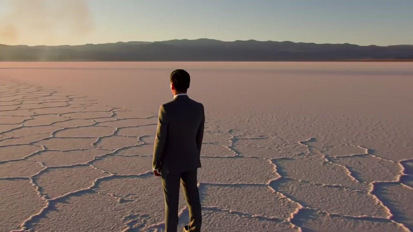 a man in a suit standing in the middle of a desert