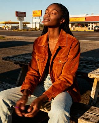 a woman sitting on a wooden bench in front of a gas station