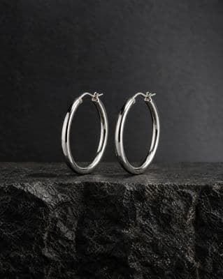 a pair of silver hoop earrings sitting on top of a rock