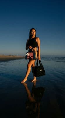 a woman walking on the beach with a handbag