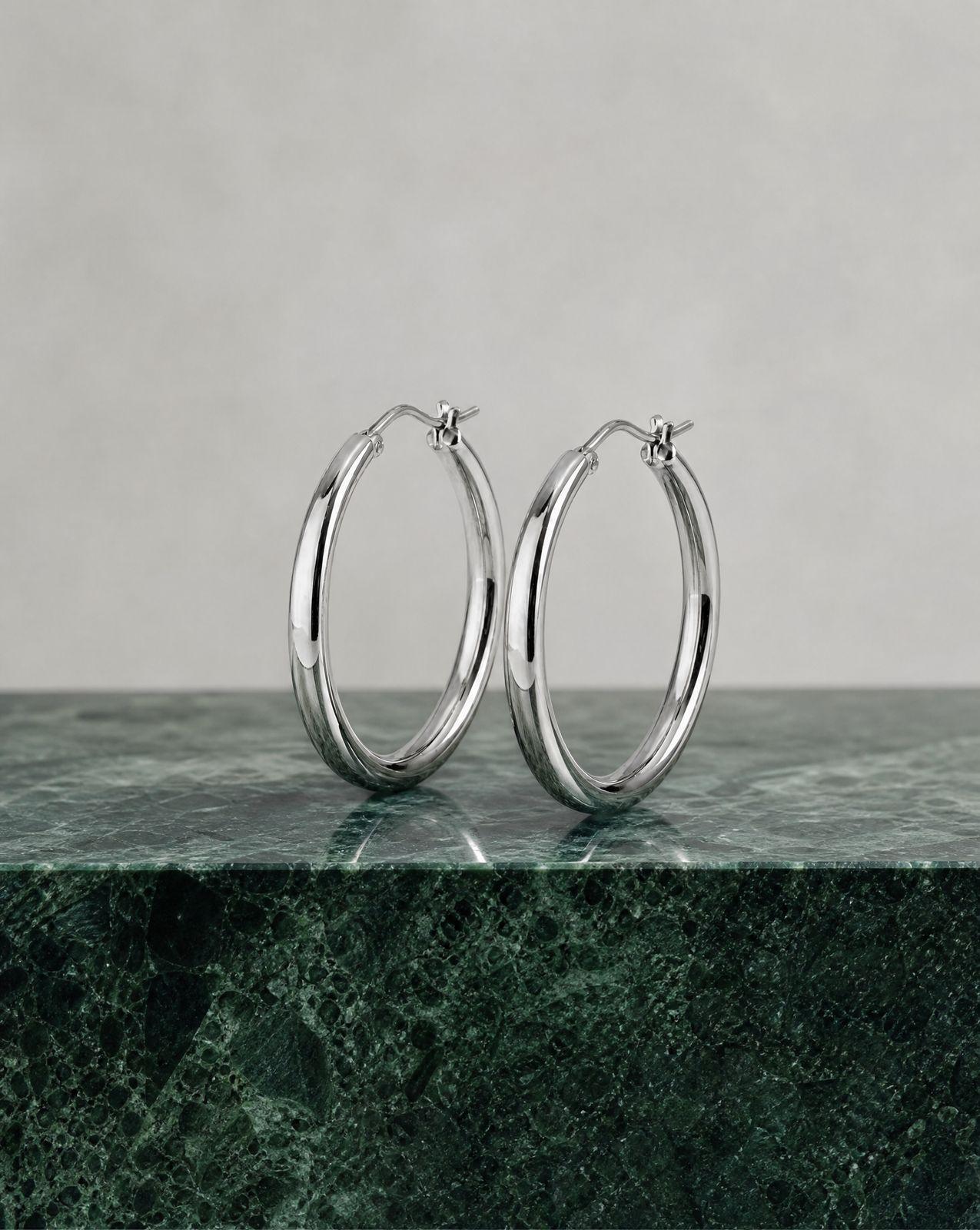 a pair of silver hoop earrings on a marble surface