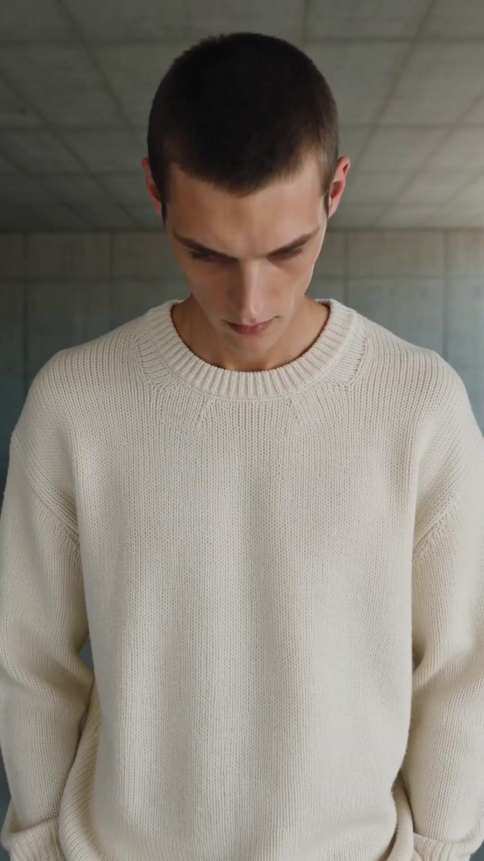 a man in a white sweater looking down at his cell phone