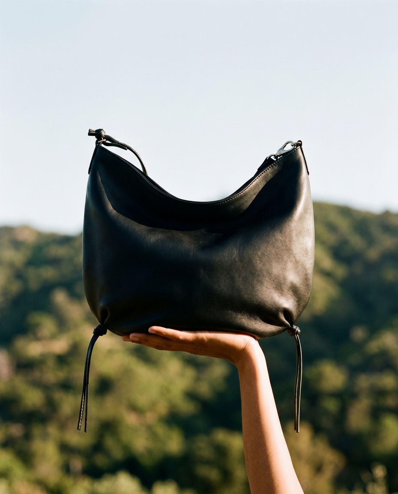 a hand holding a black purse in front of a mountain