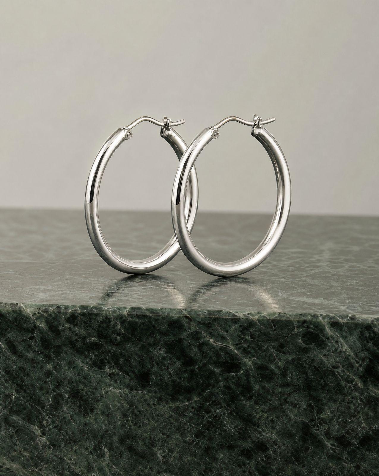 a pair of silver hoop earrings on a marble surface