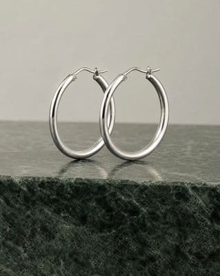 a pair of silver hoop earrings on a marble surface