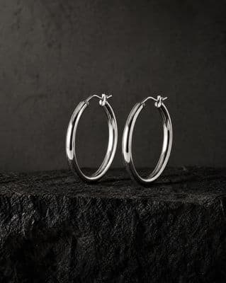 a pair of silver hoop earrings sitting on top of a rock