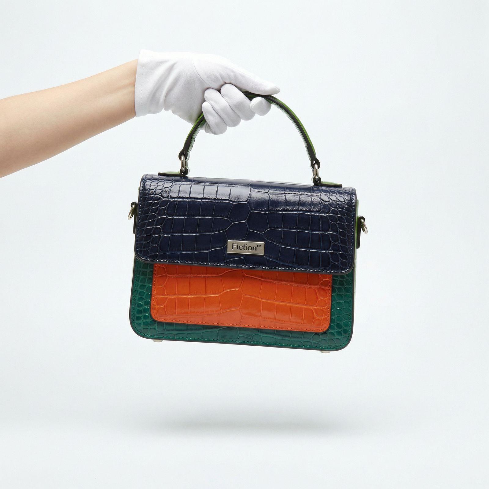 a hand in white gloves holding a blue and orange purse