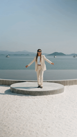 a woman in a white suit and sunglasses standing on a concrete platform