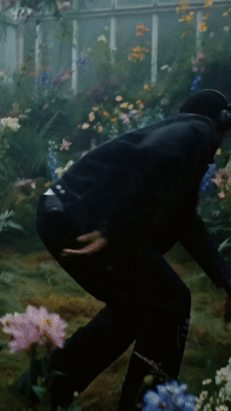 a man in a black suit and hat in a garden