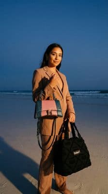 a woman standing on a beach holding a handbag