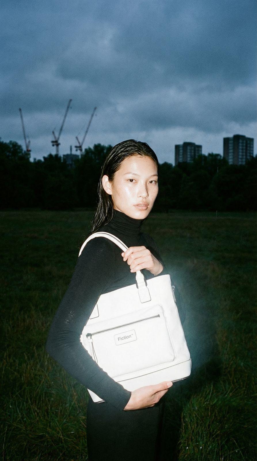 a woman standing in a field holding a white bag