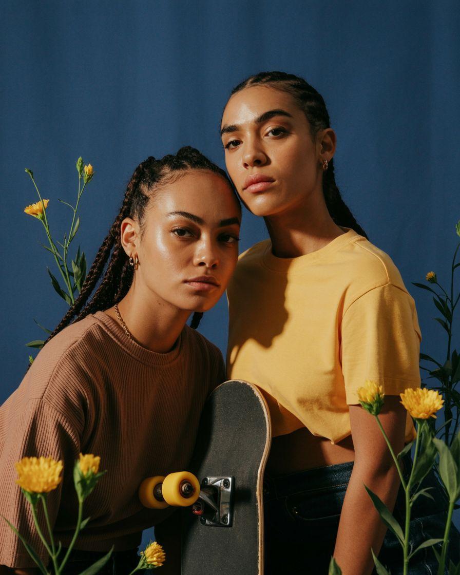 two women standing next to each other holding a skateboard