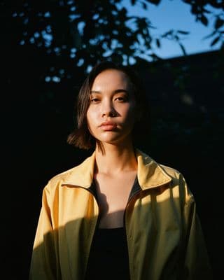 a woman standing in front of a tree wearing a yellow jacket