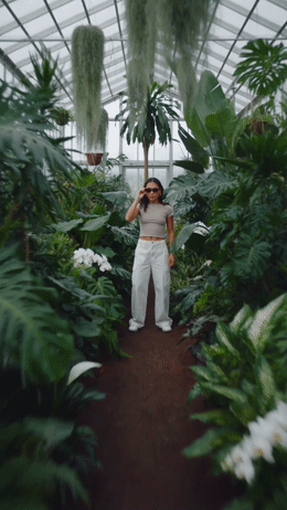 a woman standing in a greenhouse talking on a cell phone