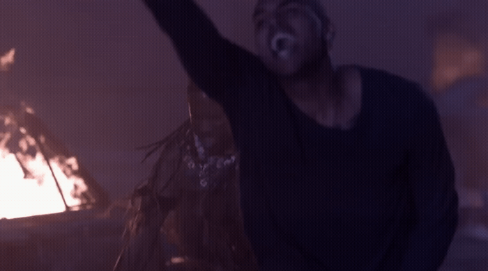 a man standing in front of a fire with his arms in the air