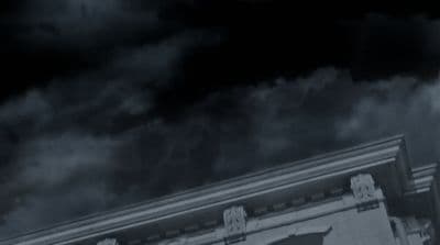 a black and white photo of a building with clouds in the background