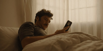 a man laying in bed looking at a cell phone