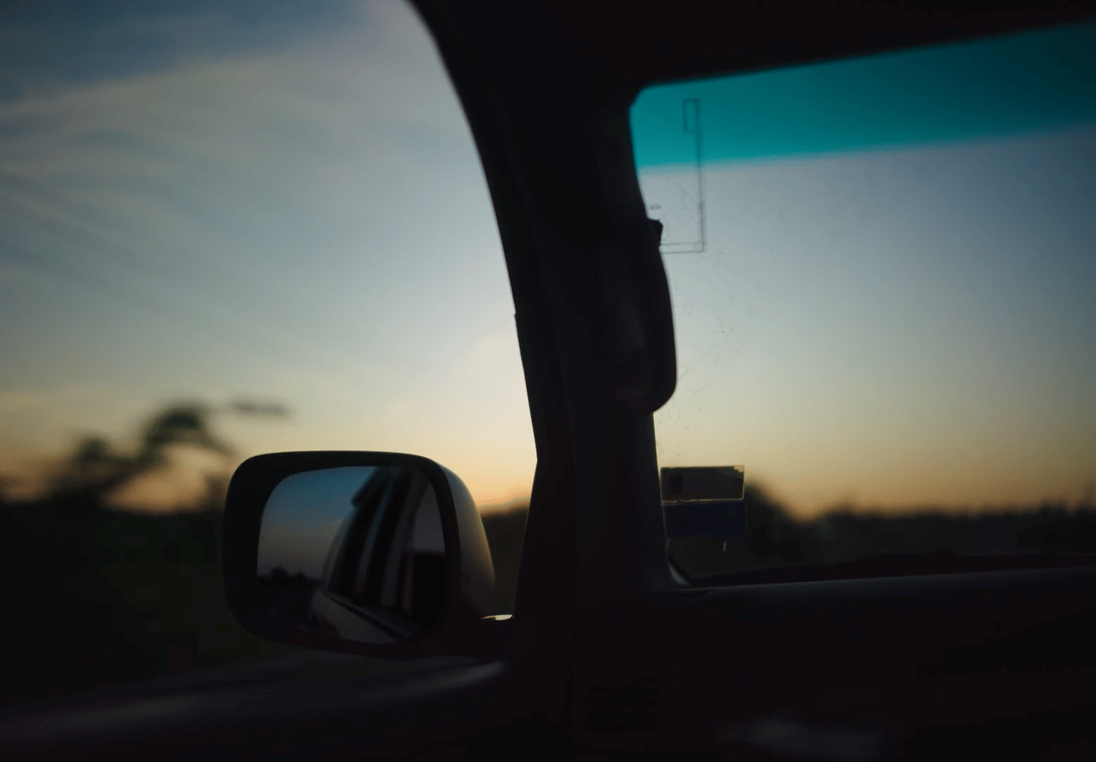a rear view mirror of a car with a sunset in the background