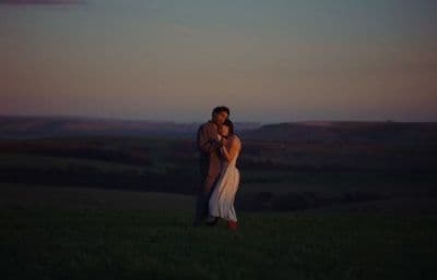 a man and a woman standing in a field at sunset