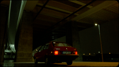 a red car parked under a bridge at night