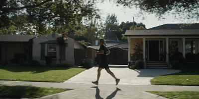 a woman running down a sidewalk in front of a house