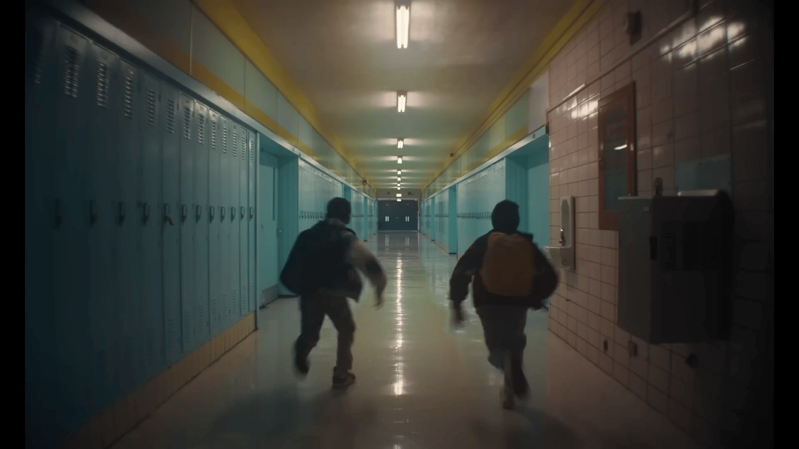 two people walking down a long hallway with lockers