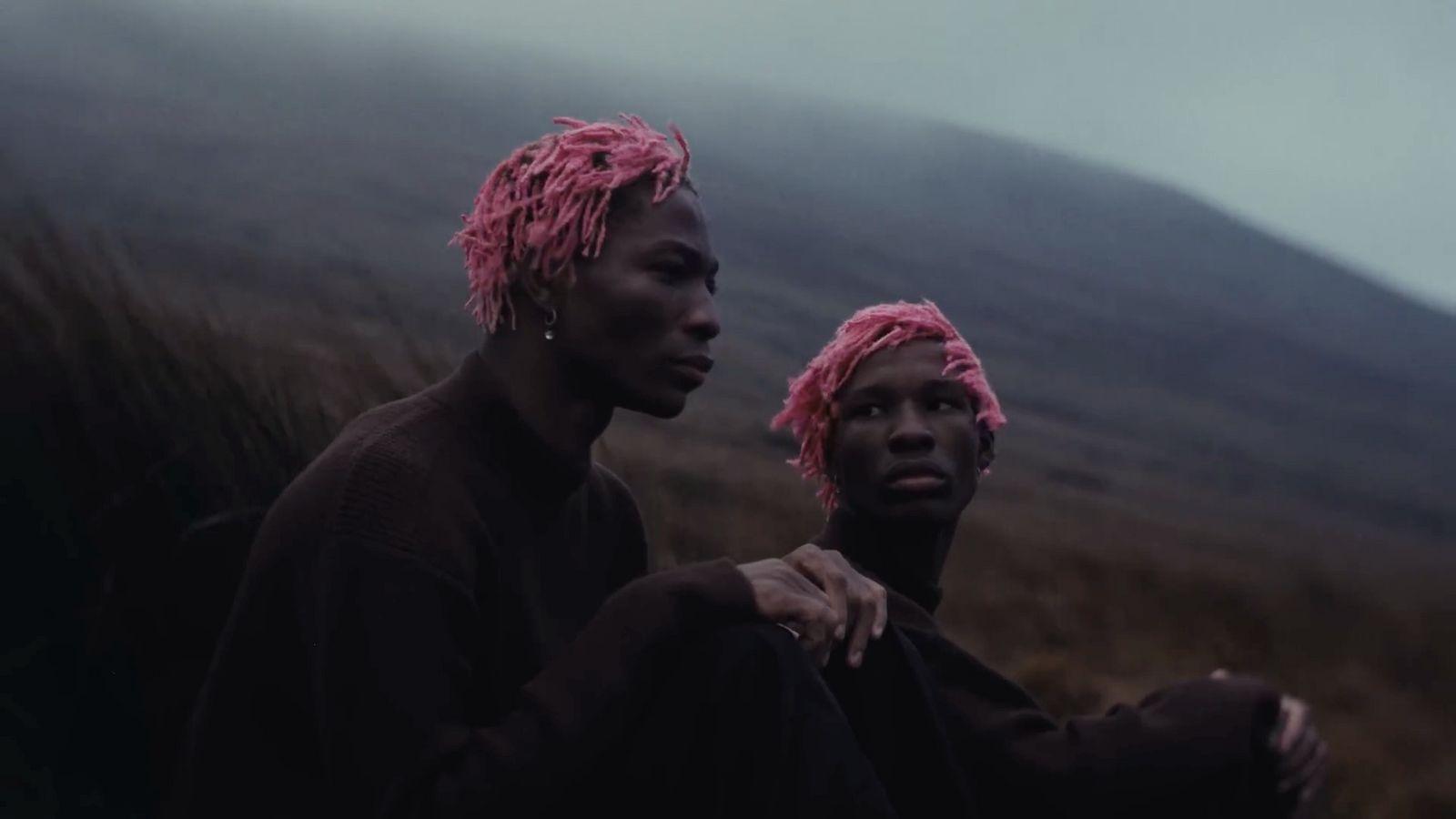 two men with pink hair sitting on a hill
