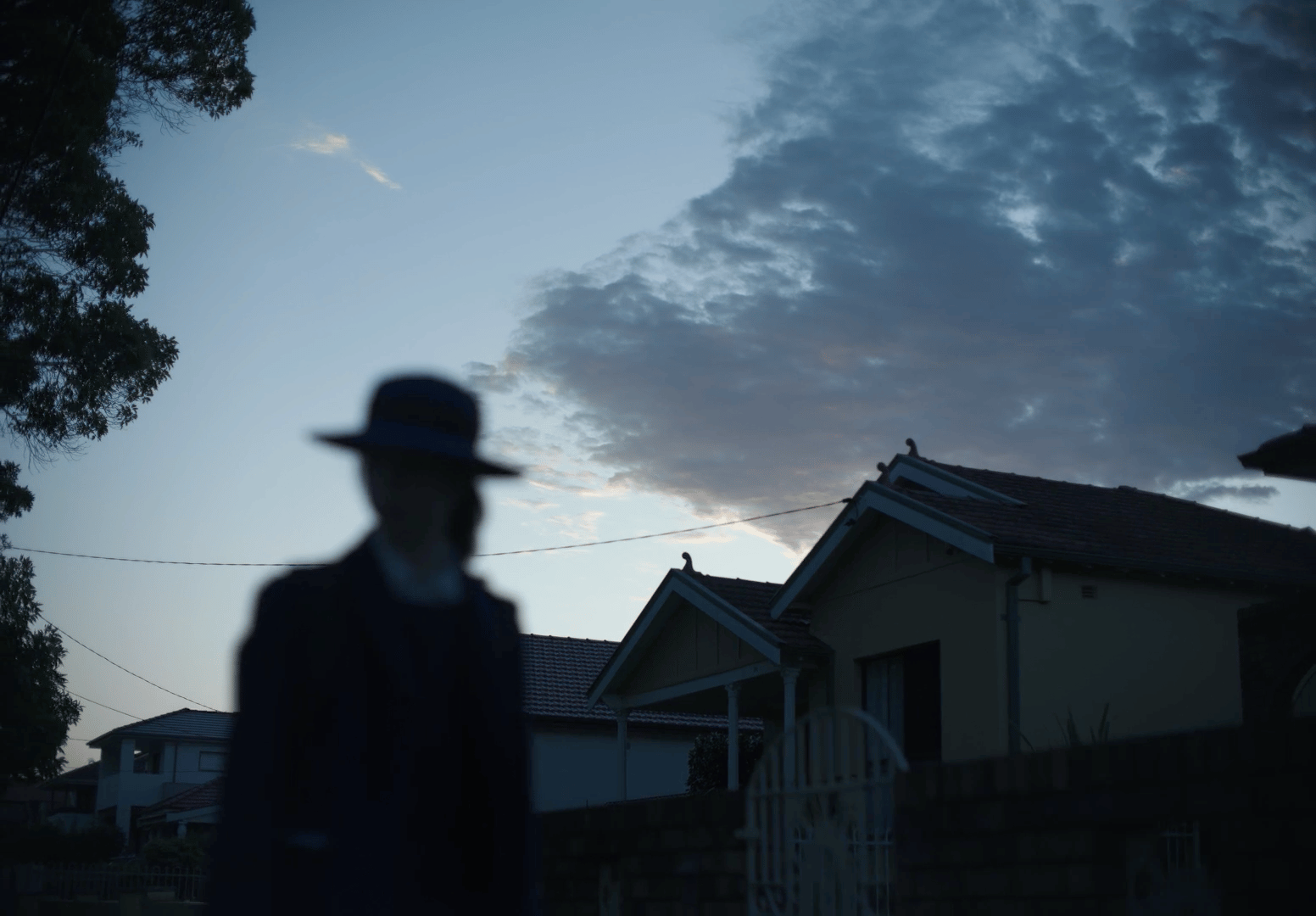 a man wearing a hat standing in front of a house