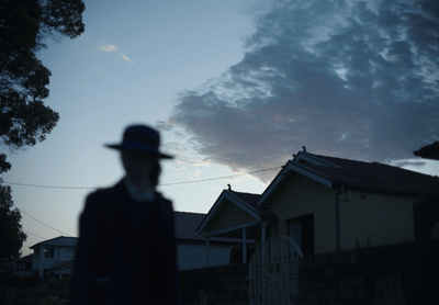 a man wearing a hat standing in front of a house