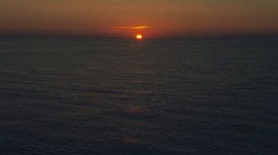 the sun is setting over the ocean on a cloudy day