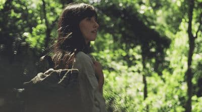a woman standing in a forest with trees in the background