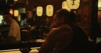 a shirtless man sitting at a bar in front of a mirror