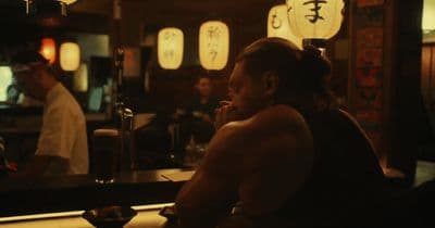 a shirtless man sitting at a bar in front of a mirror