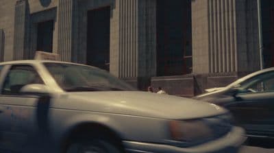 a white car driving down a street next to tall buildings