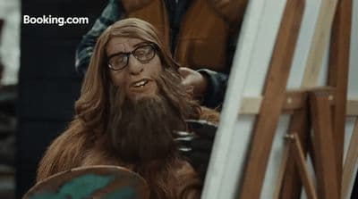 a man with long hair and glasses sitting next to a easel