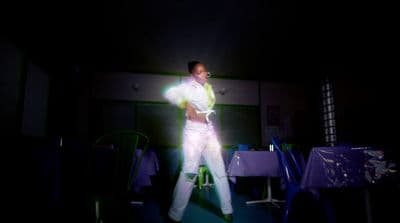 a man in a white suit is dancing in the dark