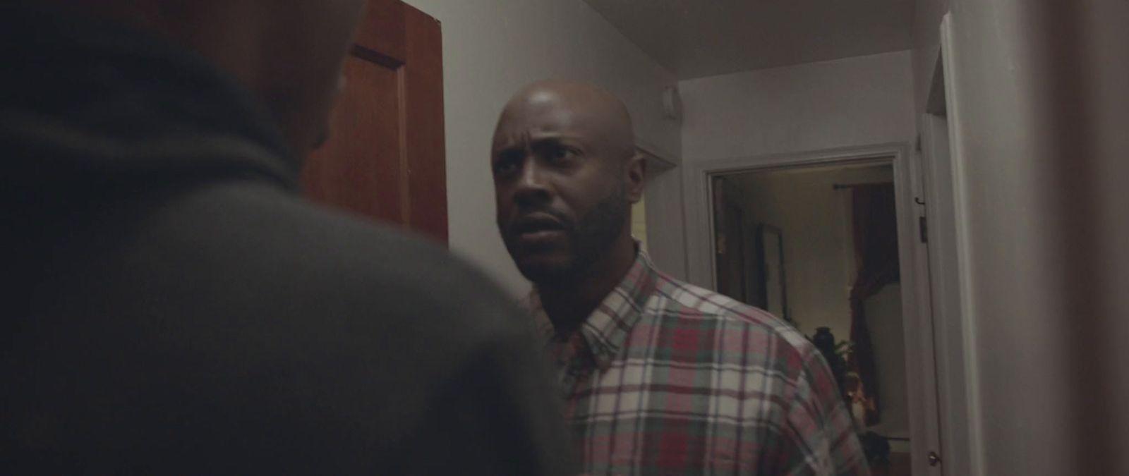 a bald man in a plaid shirt standing in front of a mirror