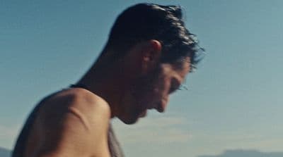 a man with no shirt on standing on a beach