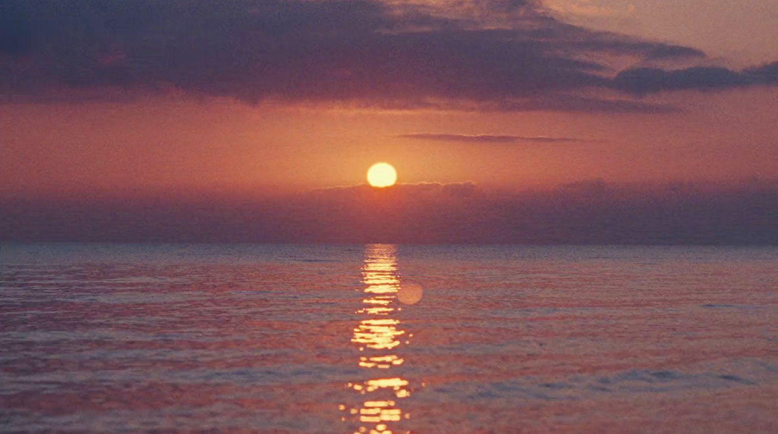 the sun is setting over the ocean on a cloudy day
