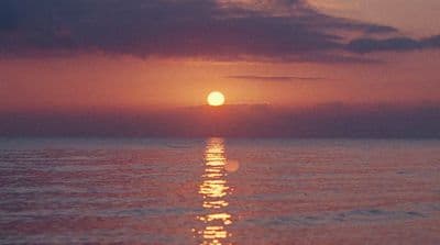 the sun is setting over the ocean on a cloudy day