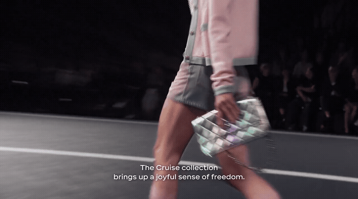 a woman walking down a runway carrying a purse