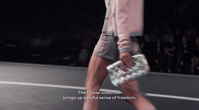 a woman walking down a runway carrying a purse
