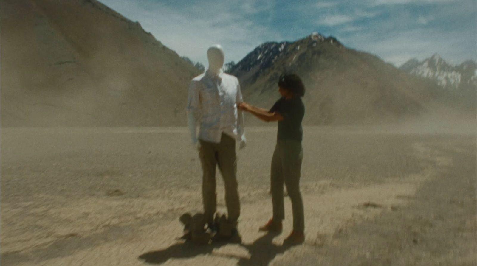 two people standing in a desert with mountains in the background