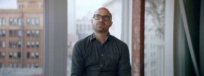a man with glasses looking out of a window