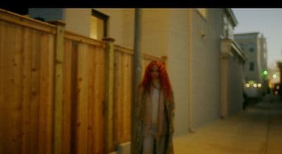 a woman with red hair standing next to a fence
