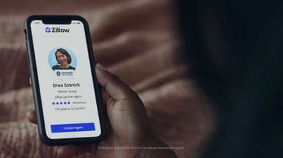 a person holding a cell phone with the zillow app on the screen