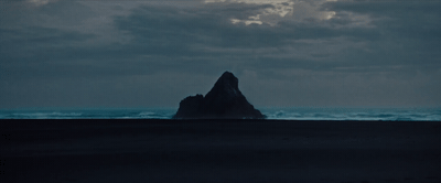 a large rock sticking out of the ocean under a cloudy sky