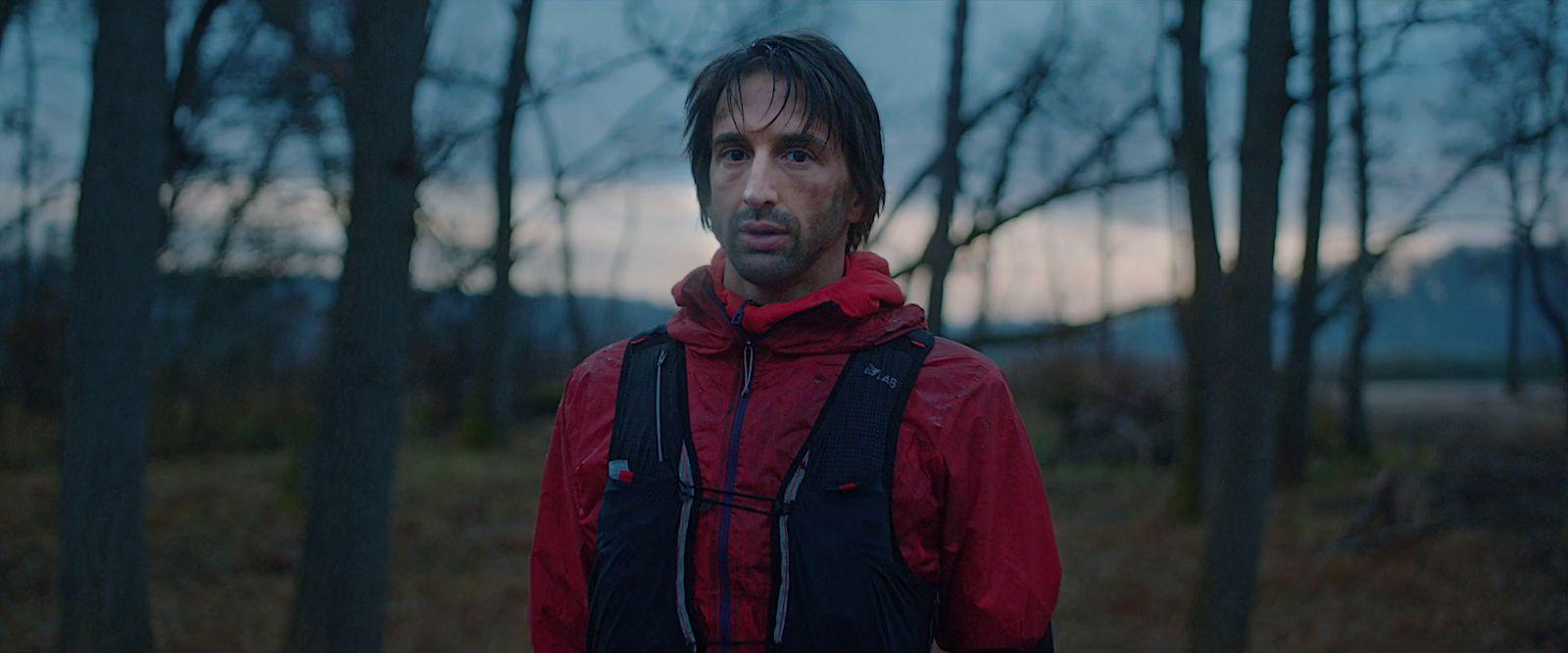 a man in a red jacket standing in a forest