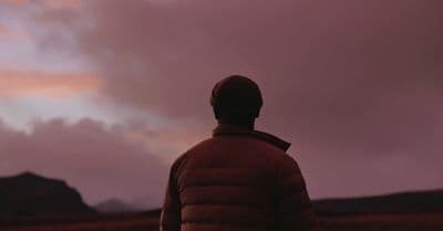 a man standing in a field looking at a cloudy sky