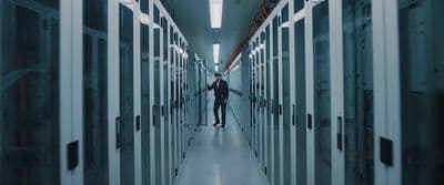 a man walking down a hallway between two rows of servers